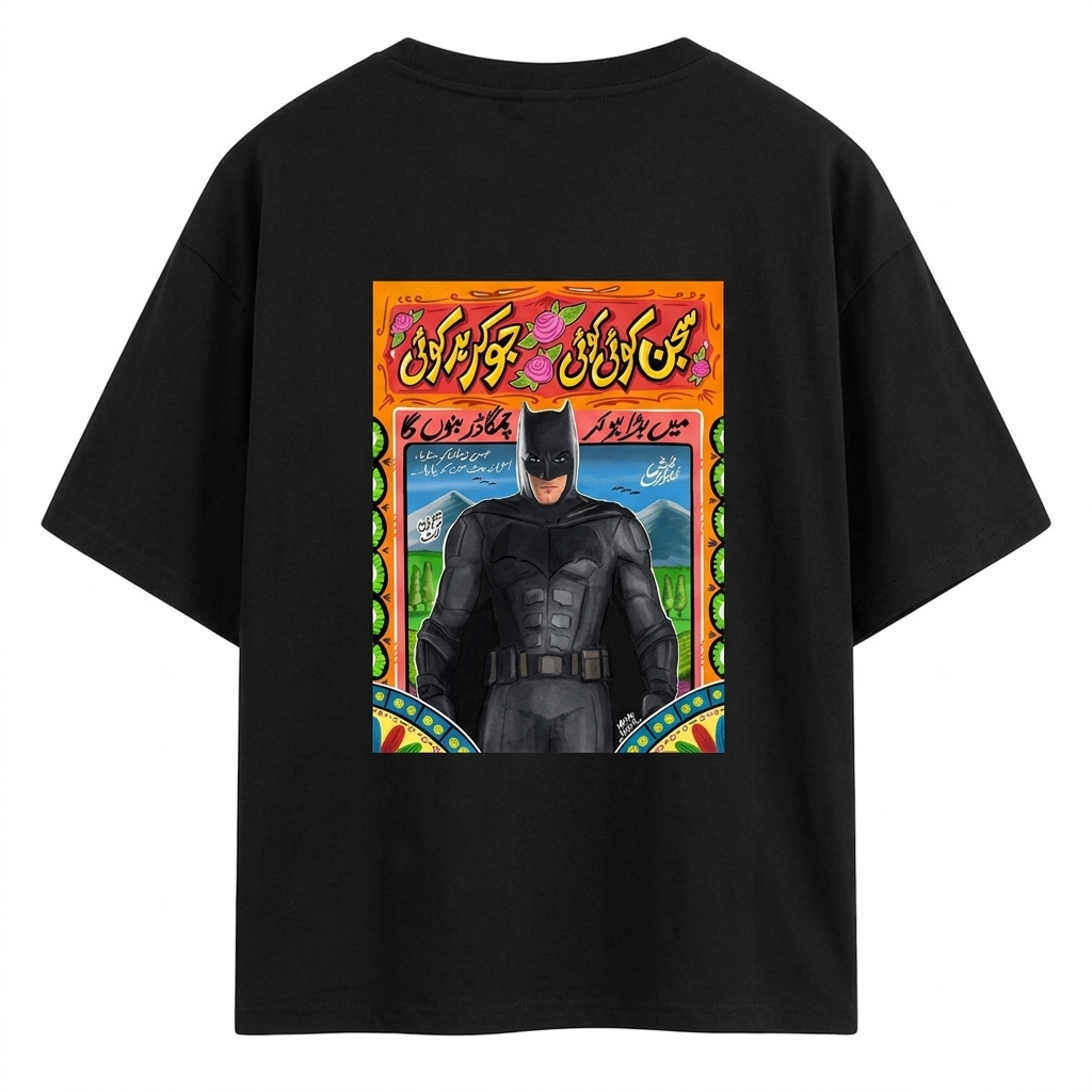 Male model wearing a black AKIDO oversized cotton graphic t-shirt featuring a colorful Batman-inspired desi truck art print with Urdu typography on the back, paired with blue jeans in a modern streetwear style